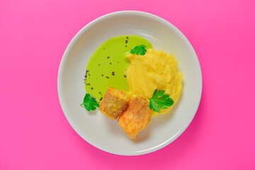 Grilled fried fish with mashed potato and sauce served in a white plate isolated on bright pink background.