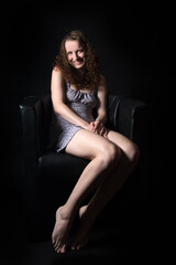 Fototapeta na wymiar Portrait of a smiling young woman sitting on a black armchair in front of black background