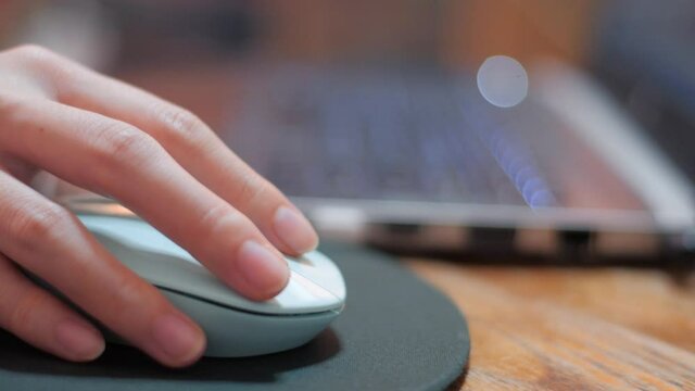 Close up of Woman is holding mouse by her hand. woman is working with laptop on wooden table. Female office worker is scrolling the pages by her.