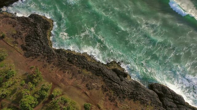 Aerial tilt down shot of lighthouse amidst green plants on cliff by sea, drone flying forward over rocky coastline on sunny day - Fingal Head Light, Australia