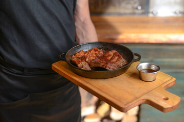 Waiter holds board with grilled meat in a pot. Spicy hot grilled meat for a BBQ. Waiter in a uniform in a restaurant.