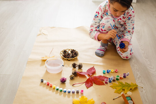 little child making autumn decoration from chestnut, pine cones and acorns