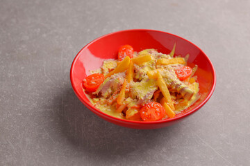 Melted cheese french fries topped off with cherry tomatoes. Served in a red bowl over gray taxtured background.