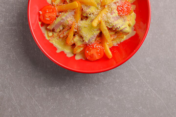Melted cheese french fries topped off with cherry tomatoes. Served in a red bowl over gray taxtured background.