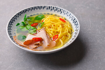 Japanese ramen soup with noodles, beef, egg, fresh parsley and sweet pepper on gray background. Copy space banner.