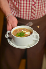 A waiter wearing plaid uniform serving a bowl of hot soup in a restaurant. Concept for a tasty and healthy meal.