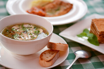 Chicken soup with vegetables and meat served in a white bowl over rustic wooden background with green plaid tablecloth.
