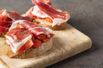 Wooden try with toasted brad slice with fresh tomatoes and cured ham. Delicious appetiser Italian...