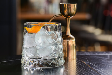 Empty whiskey glass with ice cubes and an orange twist on rustic dark wooden table in a bar or restaurant.