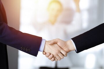 Business people shaking hands at meeting or negotiation, close-up. Group of unknown businessmen and a woman stand together in a sunny modern office. Teamwork, partnership and handshake concept