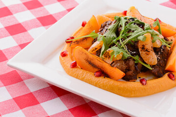 Minced meat with mashed fruit puree on white plate over red plaid tablecloth background.