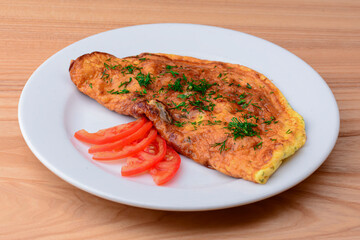 Delicious egg omelette with greens and tomatoes. Served on a white plate over light rustic wooden table background.
