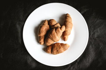 Croissants on a white plate on a black textile background. Fresh bakery