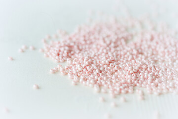Pink seed beads scattered on the textile background close up. Handmade concept