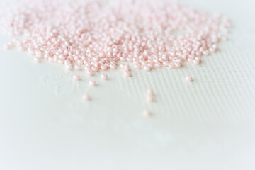 Pink seed beads scattered on the textile background close up. Handmade concept