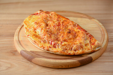 Calzone, Italian traditional food. Served on wooden board over rustic wooden table background closeup.