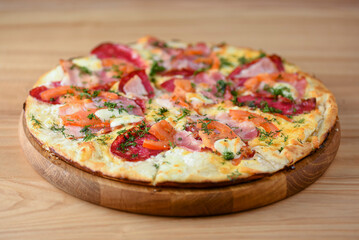 Fresh pizza with tomatoes, cheese and mushrooms on wooden board over rustic wooden table background closeup.