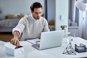 Young entrepreneur eating while using laptop at working at home.
