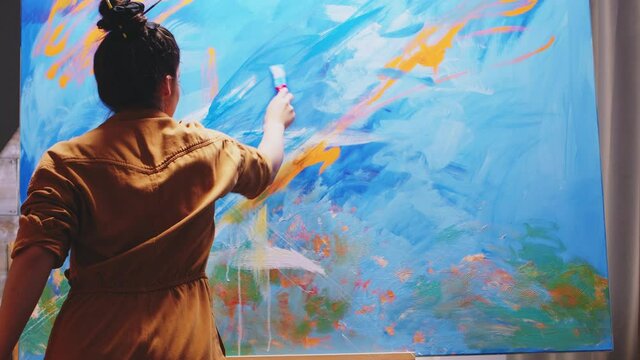 Innovative female painter using orange paint on big canvas. Modern artwork paint on canvas, creative, contemporary and successful fine art artist drawing masterpiece