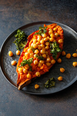 Baked sweet potato stuffed with chickpea and crunchy kale on a black plate. Vegan tasty dish for dinner or lunch.