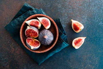 Top view of ripe figs in a wooden bowl over dark blue background.