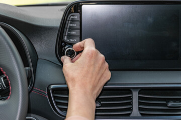 Closeup of woman hand, turning button on car radio for listening to music. Modern car interior.