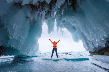 Male tourist in orange clothes on Lake Baikal, Russia. Stunning ice cave, blue background picture.