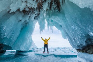 Male tourist in yellow clothes on Lake Baikal, Russia. Stunning ice cave, blue background picture.