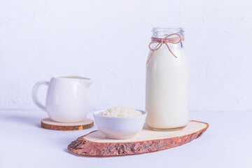 Vegan rice milk in a glass bottle and rice in a white plate on a wooden stand on a white background