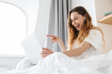 Portrait of ginger joyful woman pointing finger at laptop in bed