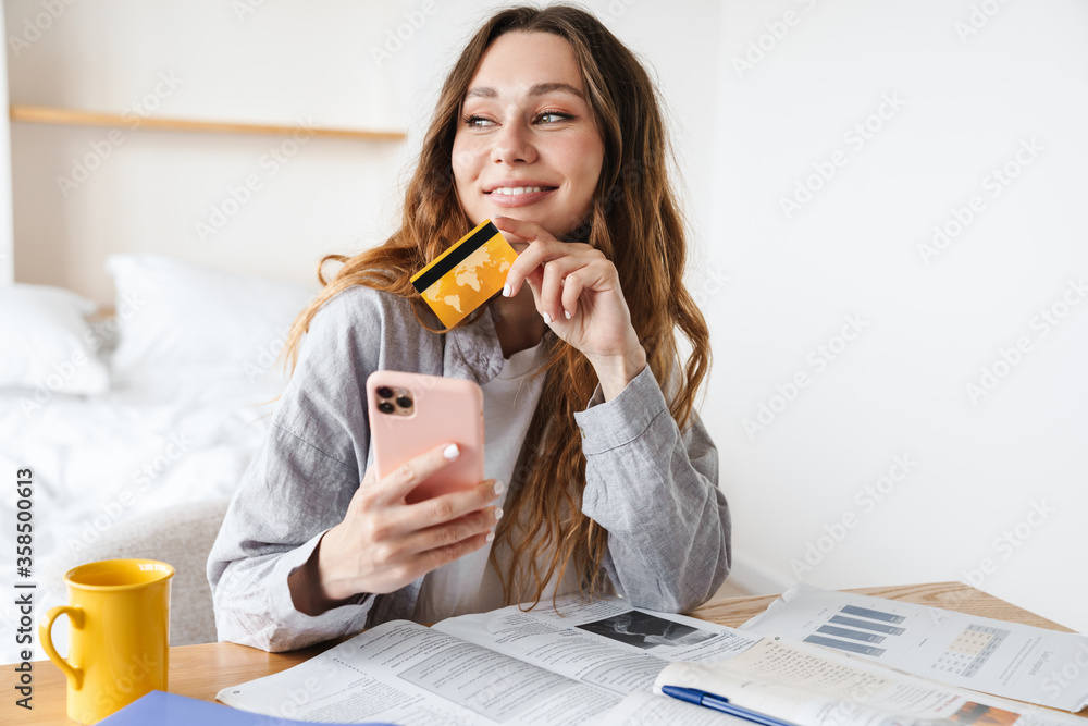 Canvas Prints Photo of woman holding credit card and smartphone while doing homework