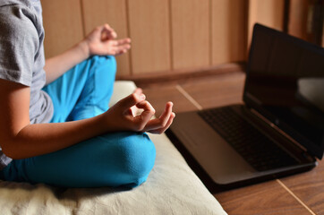 child does yoga in front of a laptop monitor. Remote classes via the Internet.