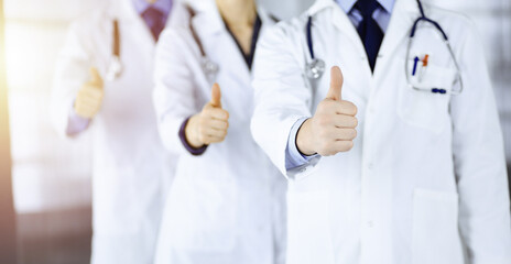 Group of unknown doctors stand as a team with thumbs up in a sunny hospital office. Physicians ready to examine and help patients. Medical help, insurance in health care, best desease treatment and