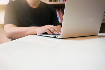 image of a young man working on his laptop in library, rear view of business man hands busy using laptop at office desk, young male student typing on computer sitting at wooden table