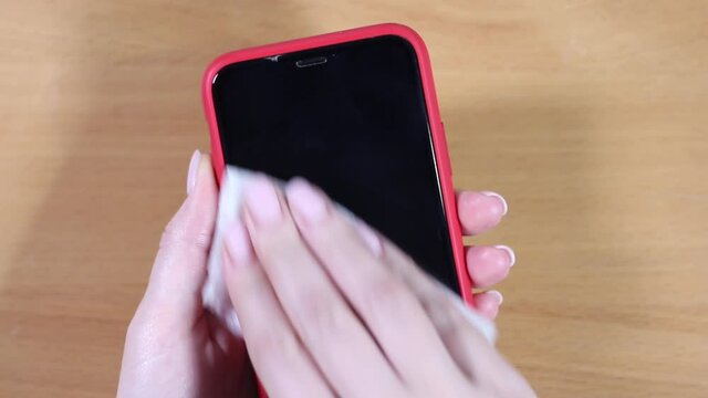 Female hands hold a smartphone in a red case and wipes the screen with a napkin