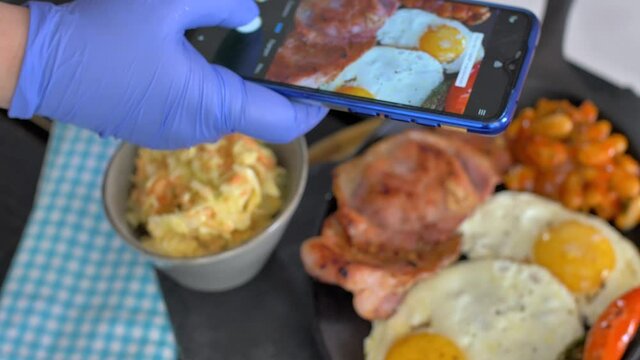 A woman in a restaurant takes a picture of food with a mobile phone camera. Sandwich with poached egg and avocado