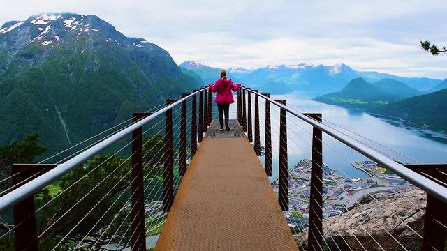 Hiking Rampestreken. Tourist girl on the Rampestreken Viewpoin. Panoramic landscape Andalsnes city located on shores of Romsdal Fjord between the picturesque mountains. Andalsnes. Norway.