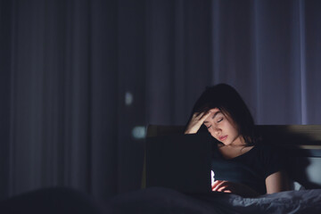 Exhausted Young business woman using laptop working late at night on bed