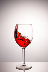 A splash of red wine in a glass on a white background