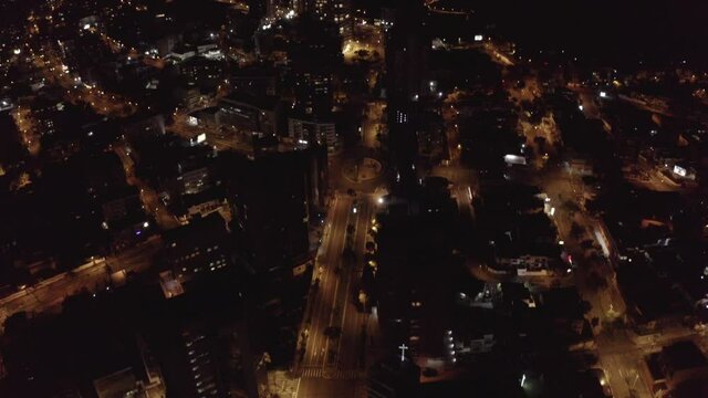 Drone shot in the night of the city of Quito, Ecuador. Overlooking empty streets with lights during quarantine. Buildings, houses and one car passing by.