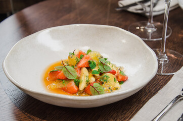 Healthy eating concept. Fresh fruit salad with strawberry, passion fruit, kiwi, peach, leaf, and micro greens with a glass of clean water on a table in a restaurant.