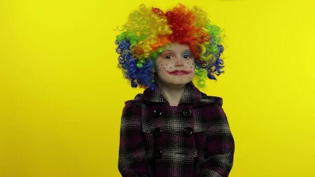 Little caucasian child girl clown in rainbow wig making silly faces, hakes her head. Halloween