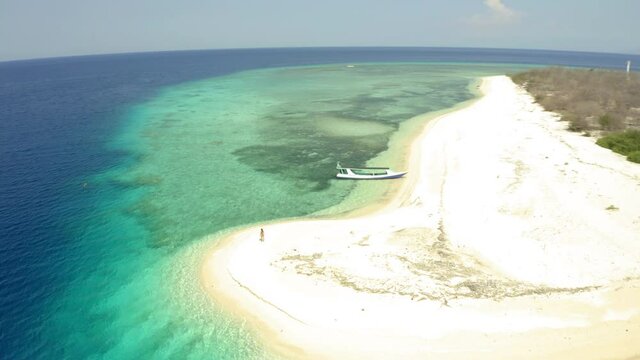 Aerial panning shot of tourists at small island against sky on sunny day, drone flying backward over sea - East Java, Indonesia
