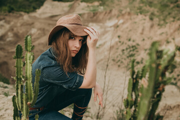 Young beautiful woman sitting on the sand in a blue denim suit and red hat in a Western style in a...