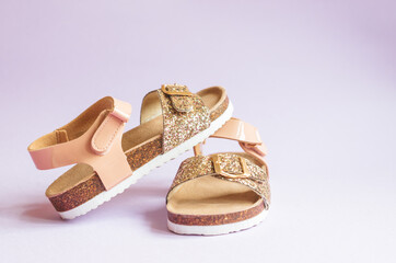 Summer sandals for children with shades of pink and gold glitter over purple background isolated.