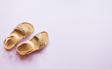Summer sandals for children with shades of pink and gold glitter over purple background isolated.