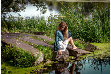 A girl sits on a lake with a hand near the water. sad woman near the water.