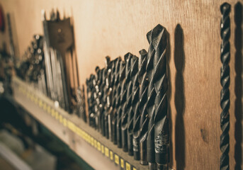 A row of drillbits, wood or metal drill, on a workbench. Wood background. Depth of field. Vintage look.