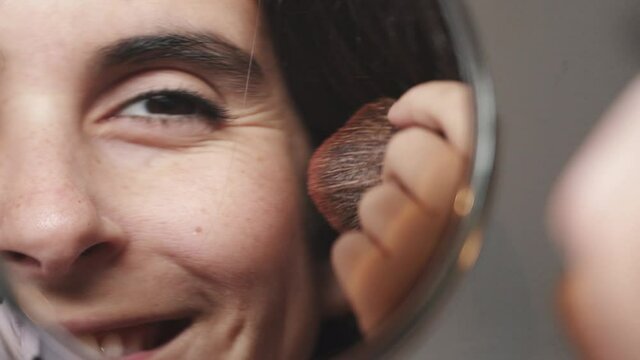 Attractive young woman  putting on makeup with brush adding blush bronzer on the face. Cosmetic concept. mirror close up