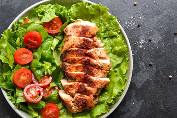 Grilled chicken breast salad with spinach and tomatoes. Healthy eating Fried chicken breast, lemon, cherry tomatoes, spinach and lettuce. Dark background. Close up.